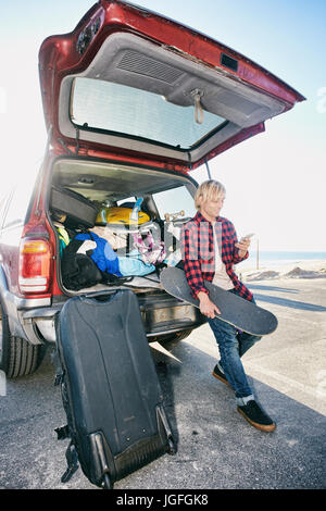 Caucasian man holding skateboard et texting on cell phone Banque D'Images