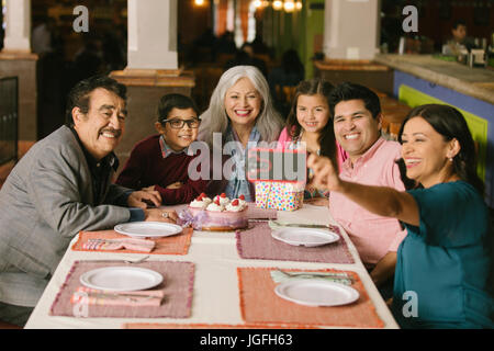 Family celebrating birthday posant pour restaurant en selfies Banque D'Images