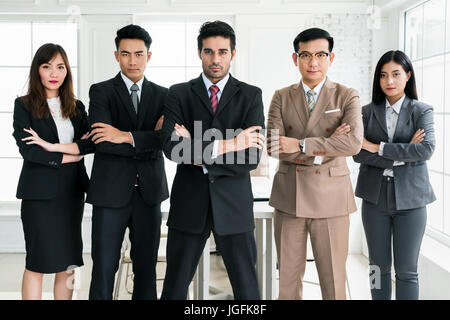 Cinq personnes d'origine ethnique muti confiant qui traversent leurs bras devant une fenêtre lumineuse. Businessman and businesswoman standing in office. Banque D'Images