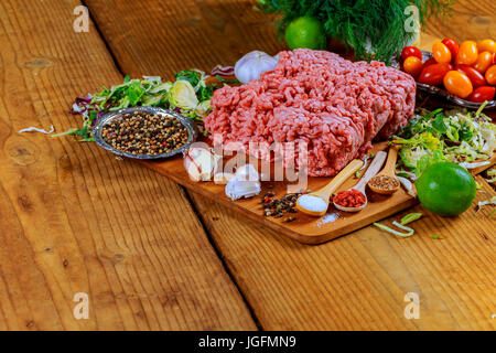 Burger de viande de boeuf haché cru escalopes steak avec assaisonnement, tomates, salade et bun sur planches de bois vintage, l'arrière-plan Banque D'Images