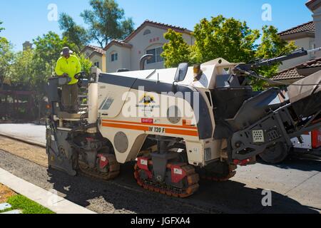 Un travailleur de la construction pour l'Asphalte américain, portant un gilet jaune, oriente une machine qu'il supprime l'asphalte lors d'un projet de revêtement routier et de construction dans la région de la baie de San Francisco suburb de San Ramon, Californie, le 26 juin 2017. Banque D'Images