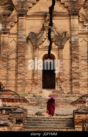 Un moine bouddhiste dans la robe rouge avec parapluie à la pagode en ruine. Banque D'Images