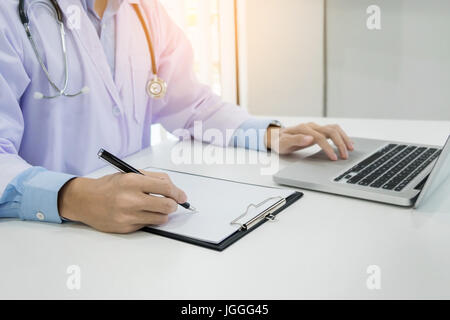 Close up of unknown médecin homme assis à la table près de la fenêtre à l'hôpital et en tapant à l'ordinateur portable Banque D'Images