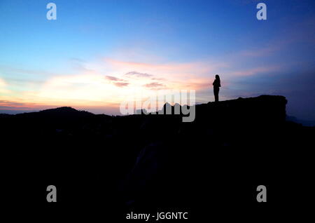 Une femme se trouve au sommet d'un volcan en regardant le lever du soleil Banque D'Images
