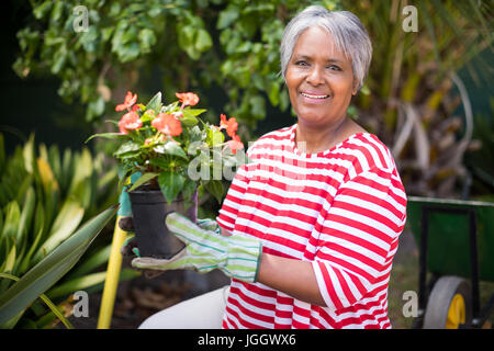 Portrait of smiling woman holding potted plant tout en s'agenouillant dans la cour Banque D'Images