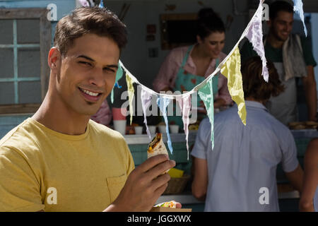 Portrait of young man eating tortilla en position debout par camion alimentaire Banque D'Images