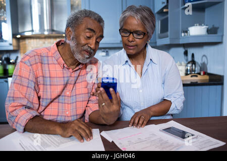 Couple using calculator en discutant par rapport au document dans la cuisine Banque D'Images
