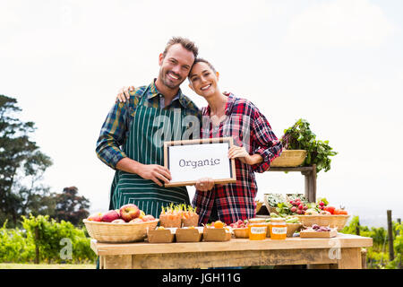 Portrait of smiling couple avec tableau noir blanc vente de légumes à la ferme Banque D'Images