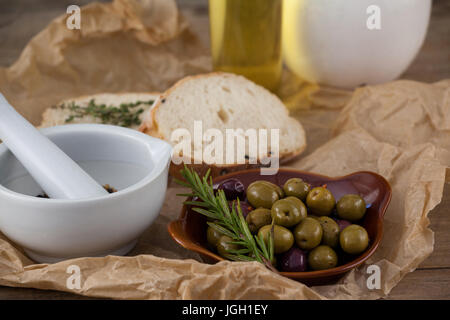 Close up de mortier pilon par les olives et le romarin dans la plaque sur papier Banque D'Images