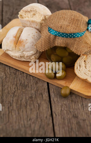 Olives en bocal avec de la jute par pain sur une planche à découper à table Banque D'Images
