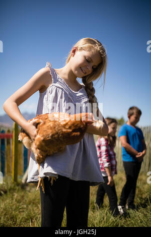 Jeune fille souriante portant une poule dans la ferme sur une journée ensoleillée Banque D'Images