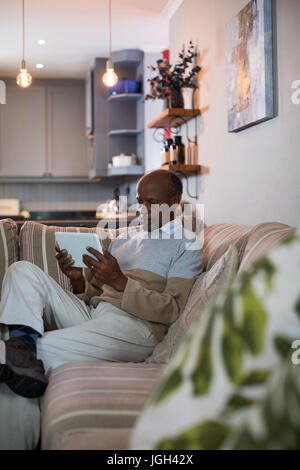 Senior man using tablet while sitting on sofa at home Banque D'Images