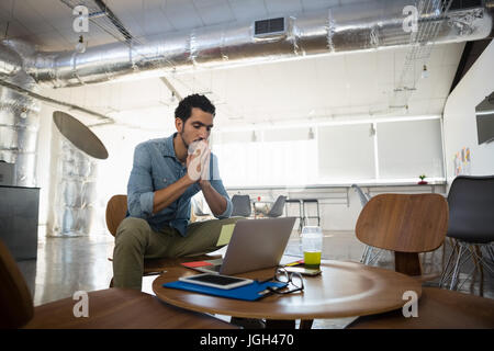 Assez jeune homme assis par table avec laptop in office Banque D'Images