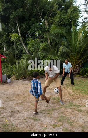 Garçon jouant au football avec les parents dans la cour sur le terrain Banque D'Images