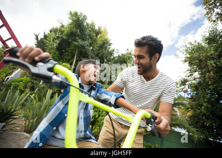 Heureux père fils aidant tout en équitation vélo contre sky in yard Banque D'Images