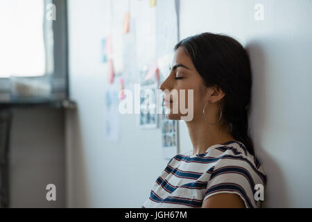 Fatigué young woman leaning on wall in creative office Banque D'Images