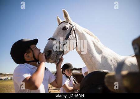 Boy kissing le cheval blanc dans le ranch sur une journée ensoleillée Banque D'Images