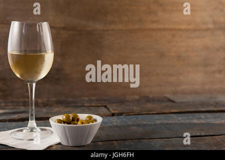 Vin blanc par green olives servi dans un récipient sur la table en bois contre le mur Banque D'Images