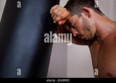 Fatigué man punching bag in fitness studio Banque D'Images