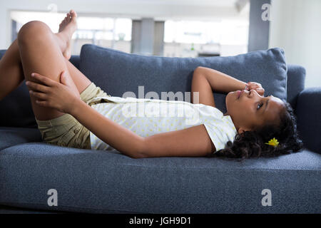 Vue latérale du thoughtful girl lying on sofa in living room à la maison Banque D'Images
