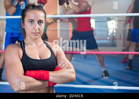Portrait of female boxer standing with arms crossed contre ring de boxe Banque D'Images