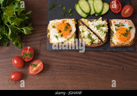 Toast à l'avocat. Petit déjeuner sain. Vue d'en haut. Sandwich fait maison avec de l'avocat et d'Œufs frits, concombres et tomates cerises sur un fond de bois. Fo foncé Banque D'Images