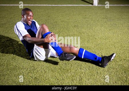 Jeune joueur de soccer masculin de crier à l'agonie avec une douleur au genou sur le terrain de jeu Banque D'Images