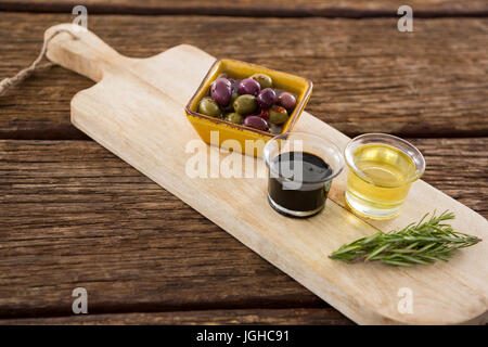 Close-up of olive mariné, le romarin avec de l'huile d'olive et de vinaigre balsamique sur plateau en bois Banque D'Images