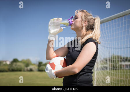 Le joueur de soccer féminin assoiffé d'eau potable sur terrain au cours de journée ensoleillée Banque D'Images