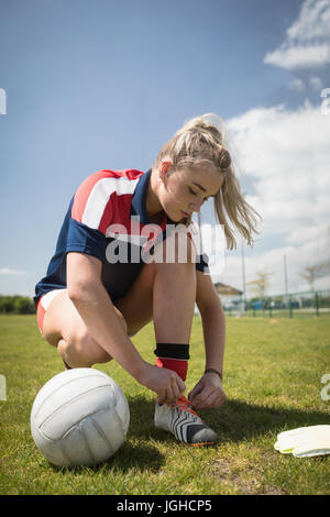 Jeune femme avec ballon de football de gardien de lacet de liage sur terrain against sky Banque D'Images