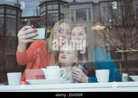 Smiling pregnant woman and friends sur téléphone mobile en selfies restaurant Banque D'Images