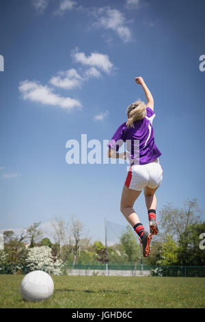 Vue arrière pleine longueur du joueur de soccer féminin de sauter sur domaine against sky