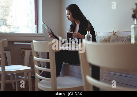 Beautiful woman reading newspaper in restaurant Banque D'Images