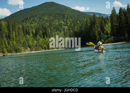 Vue de moyenne distance couple matrue kayak dans le lac de montagne contre l'arbre Banque D'Images