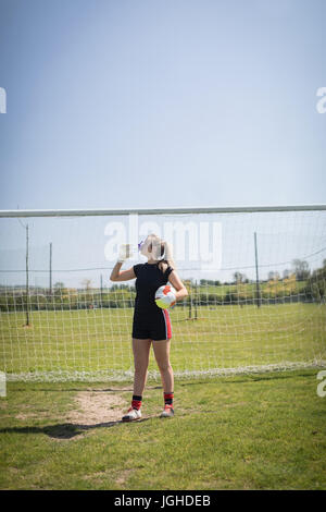 Le joueur de soccer féminin de l'eau de boisson contre poteau de but sur terrain au cours de journée ensoleillée Banque D'Images