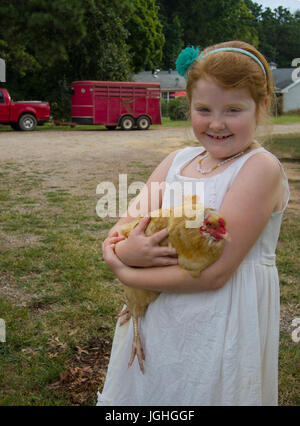 Red Headed young girl holding hen on farm Banque D'Images