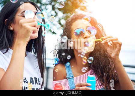 Deux jeunes copines sans souci de s'amuser ensemble faire des bulles avec un jouet bubble wand tout en profitant d'une journée ensoleillée à l'extérieur ensemble Banque D'Images