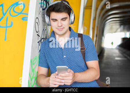 Young Man Wearing Headphones Using Mobile Phone In Urban Setting Banque D'Images