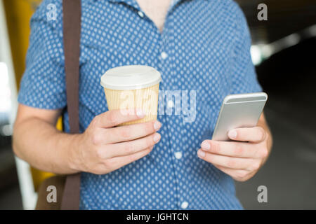 Close Up of Man avec du café à emporter des SMS sur téléphone mobile Banque D'Images