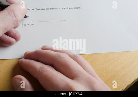 La main de signature de 'Signature' sur la ligne pointillée d'un document juridique blanc avec cartouche stylet, tandis que l'autre main repose sur la lumière Banque D'Images
