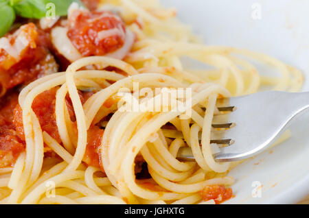 Un bol de pâtes, sauce tomate et les feuilles de basilic avec du fromage. Close-up de l'enroulement de la fourche et d'élever les spaghettis en premier plan. Banque D'Images