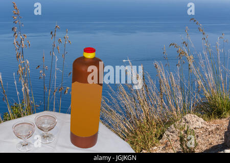 Bouteille en céramique avec deux liqueurs sur une petite table dans l'arrière-plan le bleu de la mer et un bateau sport. Banque D'Images