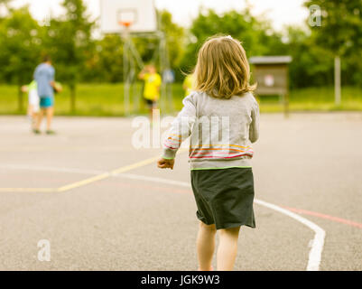 Petite fille courir vers plus grands garcons jouant des sports dans un terrain de basket ball Photo Stock Alamy