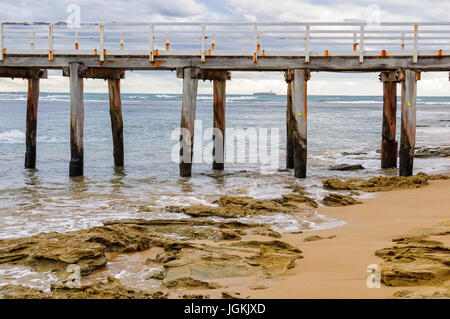 Vieux piliers de la jetée de Point Lonsdale avec un porte-conteneurs à l'horizon - Victoria, Australie Banque D'Images