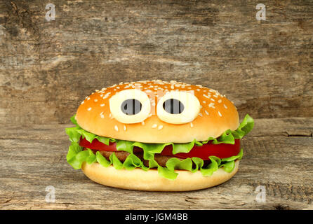 Funny Big hamburger au fromage avec les yeux sur fond de bois Banque D'Images