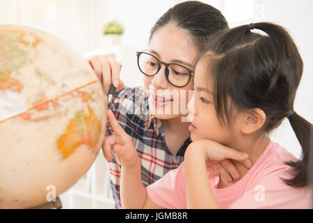 Jolie maman homeschooling heureux fille intelligente de l'enseignement leçons privées en Asie. globe fille gravement les enfants à toucher la carte et curieux à regarder. Banque D'Images