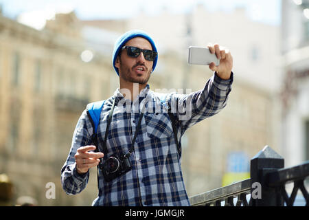 Ce jeune homme tout en ayant des selfies à pied dans la ville Banque D'Images