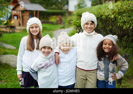 Heureux les enfants d'âges divers comité permanent près l'un de l'autre et à la caméra à sourire, vêtu de vêtements en tricot blanc qui se présentent comme des frères et sœurs ou fam Banque D'Images