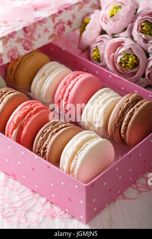 Macarons de fête dans une boîte-cadeau et de fleurs sur une table. La verticale Banque D'Images