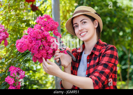 Fille jardinier fleurs de fraisage avec des sécateurs dans le jardin. Jeune femme en prenant soin de les rosiers. Les gens, le jardinage, le soin des fleurs, concept passe-temps Banque D'Images